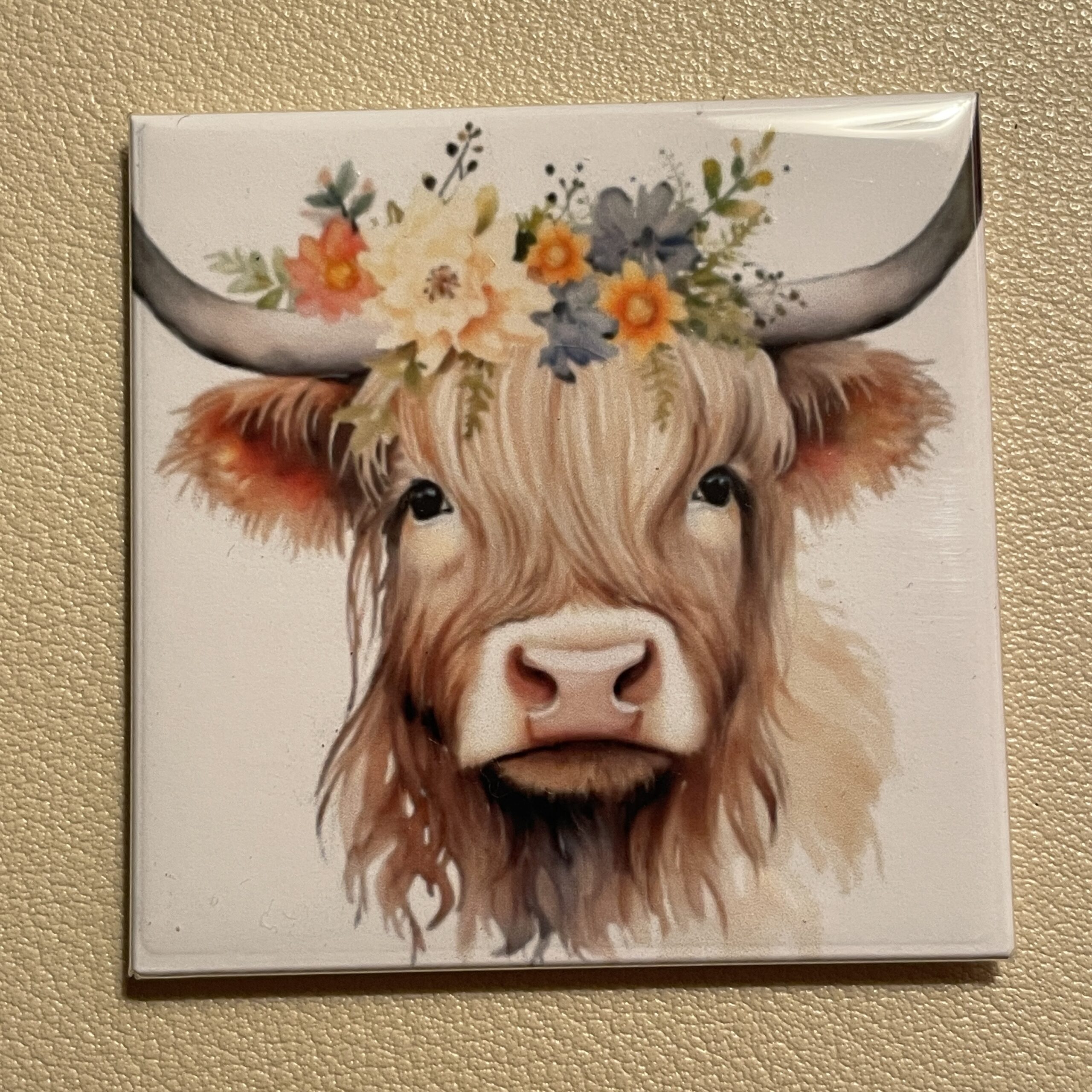 A decorative tile featuring a Highland cow adorned with a floral crown, emphasizing its gentle expression and intricate details.