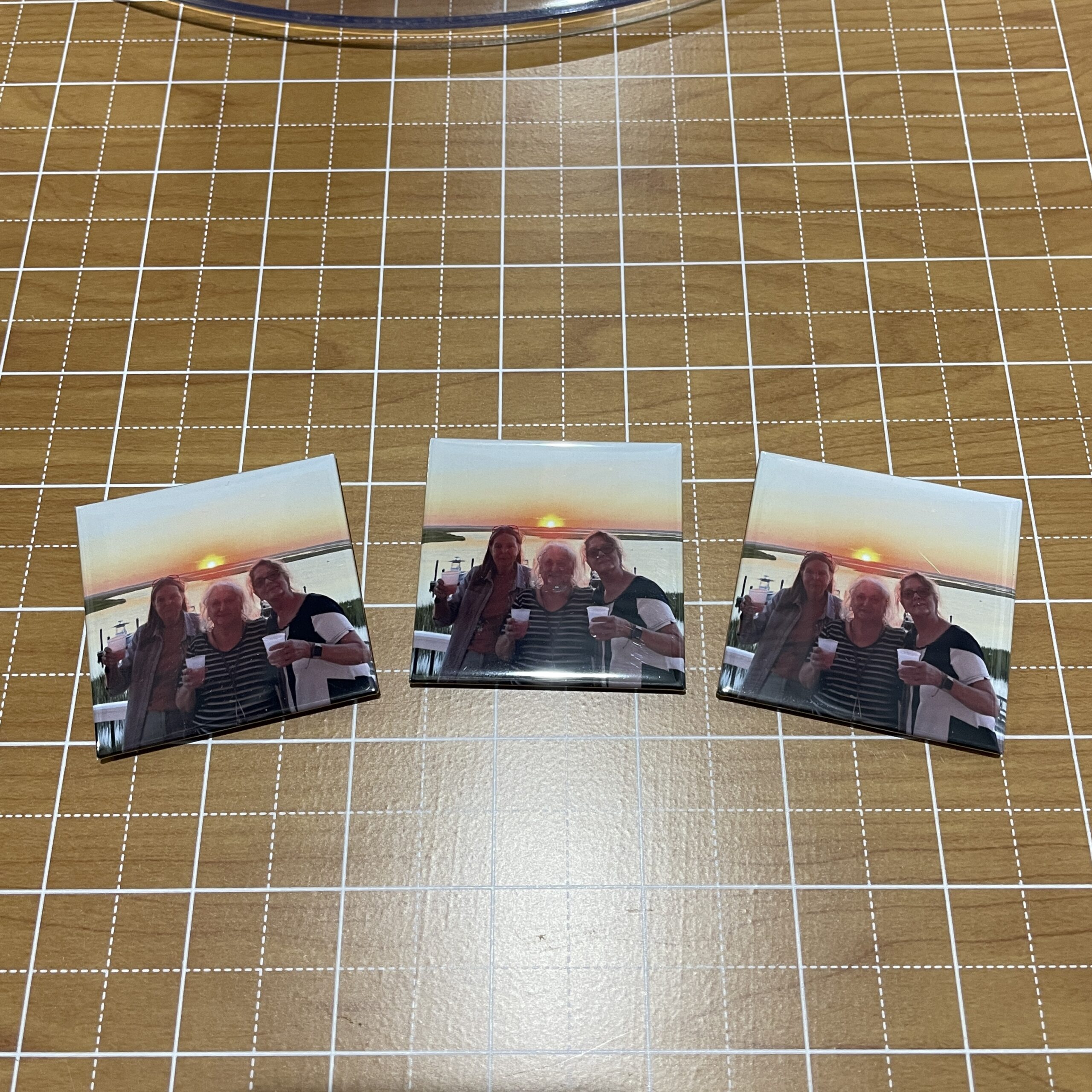 Three printed photos featuring two women and an elderly man holding drinks, posed against a sunset backdrop by a body of water.
